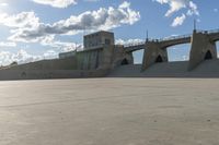 a concrete bridge spanning the width of a skateboard park and ramps under the sun and clouds