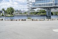 an empty parking lot next to a large bridge with people in the background and many bushes and bushes