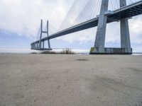 the underside of a large bridge over water in the countryside under a cloudy sky is shown