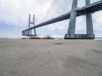 the underside of a large bridge over water in the countryside under a cloudy sky is shown