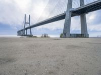 the underside of a large bridge over water in the countryside under a cloudy sky is shown