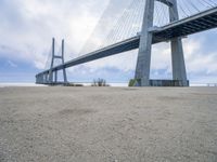 the underside of a large bridge over water in the countryside under a cloudy sky is shown