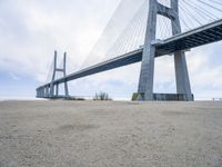 the underside of a large bridge over water in the countryside under a cloudy sky is shown