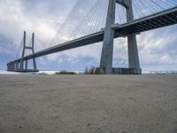 the underside of a large bridge over water in the countryside under a cloudy sky is shown