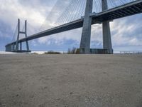 the underside of a large bridge over water in the countryside under a cloudy sky is shown