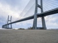 the underside of a large bridge over water in the countryside under a cloudy sky is shown