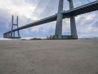 the underside of a large bridge over water in the countryside under a cloudy sky is shown