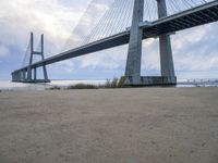 the underside of a large bridge over water in the countryside under a cloudy sky is shown