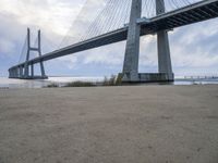 the underside of a large bridge over water in the countryside under a cloudy sky is shown