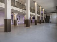 empty white, clean room with columns and light pillars in it a staircase leads to an upper floor of the room