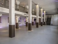 empty white, clean room with columns and light pillars in it a staircase leads to an upper floor of the room