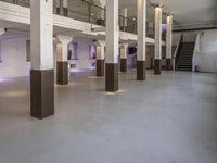 empty white, clean room with columns and light pillars in it a staircase leads to an upper floor of the room