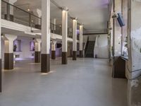 empty white, clean room with columns and light pillars in it a staircase leads to an upper floor of the room