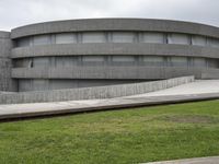 a building with cement roof near green grass and lawn in front of it, under a gray sky