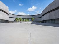 a concrete building with palm trees and white clouds in the background over an empty parking lot