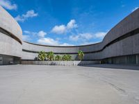 a concrete building with palm trees and white clouds in the background over an empty parking lot