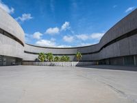 a concrete building with palm trees and white clouds in the background over an empty parking lot