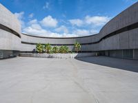 a concrete building with palm trees and white clouds in the background over an empty parking lot