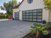 a large garage has sliding glass doors, and has green plants growing on the concrete and concrete