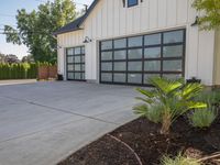 a large garage has sliding glass doors, and has green plants growing on the concrete and concrete