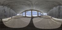 an arched concrete building next to a snow covered mountain in wintertime viewed from inside