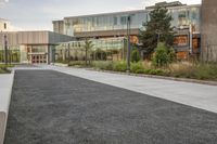 a city street surrounded by grass and tall buildings at the end of a street there is a paved pathway in front of the building