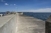 a large concrete fence along the water's edge with sculpture in distance on a clear day