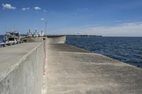 a large concrete fence along the water's edge with sculpture in distance on a clear day