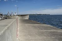 a large concrete fence along the water's edge with sculpture in distance on a clear day