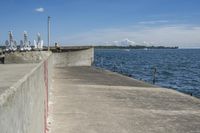 a large concrete fence along the water's edge with sculpture in distance on a clear day