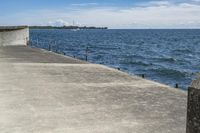 a large concrete fence along the water's edge with sculpture in distance on a clear day