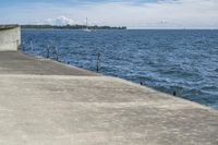 a large concrete fence along the water's edge with sculpture in distance on a clear day