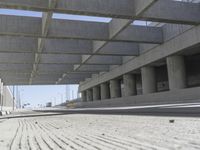 a concrete garage with large columns and a concrete wall and road area in the background