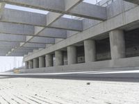 a concrete garage with large columns and a concrete wall and road area in the background