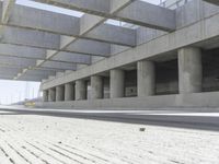 a concrete garage with large columns and a concrete wall and road area in the background