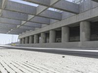 a concrete garage with large columns and a concrete wall and road area in the background