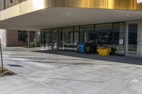 empty street in front of building with sidewalk and trashcans near side the entrance