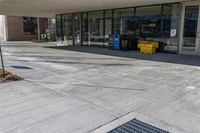 empty street in front of building with sidewalk and trashcans near side the entrance