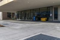 empty street in front of building with sidewalk and trashcans near side the entrance