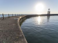 a pier with some light poles by the water with a sky background and sunbeam