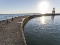 a pier with some light poles by the water with a sky background and sunbeam