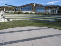 a concrete skateboard ramp going up the side of a hill by some stairs in front of a house