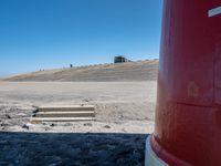 red fire extinguistor in open field by mountain side with steps to it