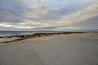 a concrete road in front of the sea with a bench at the end of it