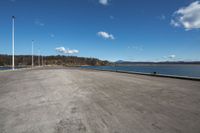 empty concrete road by the ocean with cloudy skies over it and a blue sky behind