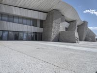 a skateboarder stands on the concrete slab outside the building's entrance, with large windows open