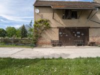 an old brown building with a bunch of white flowers on the ground and grass around it