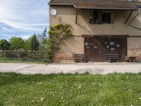 an old brown building with a bunch of white flowers on the ground and grass around it