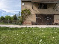 an old brown building with a bunch of white flowers on the ground and grass around it