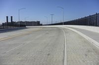 an empty freeway with two lanes with lights over the street and buildings behind it and two lanes on each side,